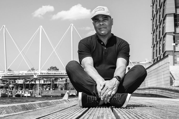 Norman Sedney, in kleermakerszit op een houten kade.